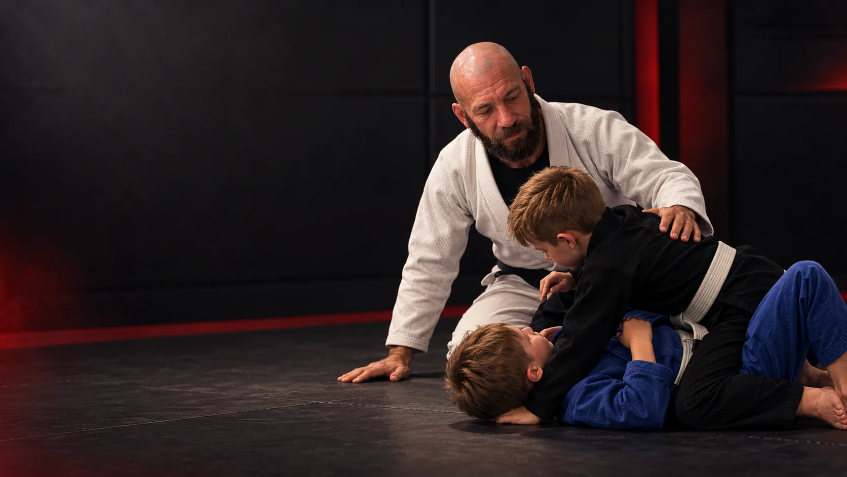 Saul guiding two children through a Jiu-Jitsu training interaction.